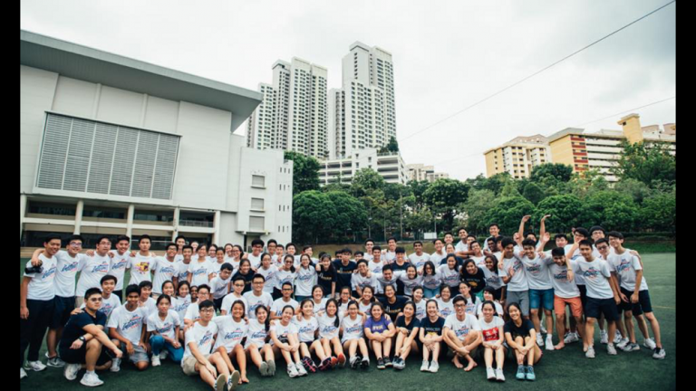 A large group of ACS(I) Interact Club members poses for a group photo outside a school or community building during an overseas service trip.